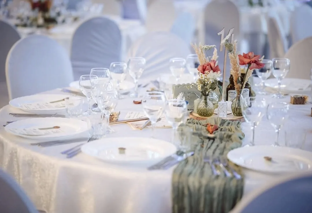 Masă rotundă pentru invitații la nuntă, decorată cu pahare de cristal, trandafiri roșii și număr de masă elegant